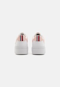 Baskets plateformes blanches avec une tige en synthétique rose. Présentent un accent rayé noir et rouge au niveau du talon et un logo en relief sur la semelle.