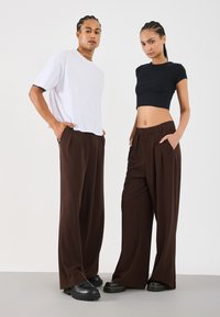 Witte oversized t-shirt en zwarte crop top gecombineerd met hoge taille bruin wijde broek, die zacht materiaal en geplooid ontwerp toont.