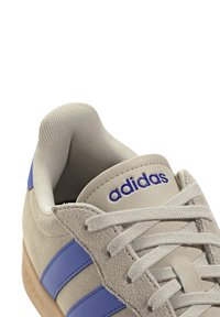 Sneaker in camoscio grigio con strisce in pelle blu, dotata di un colletto imbottito, lacci grigi chiari e logo "adidas" in viola sulla linguetta.