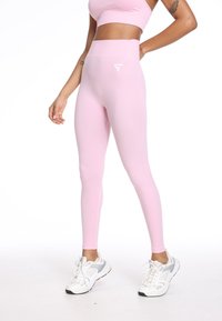 Svetlo roza leggingi z visokim pasom in brezšivno zasnovo, z majhnim belim logotipom na levem boku ter gladko, raztegljivo teksturo.