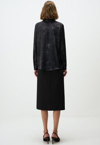 Black blouse with floral pattern in a satin-like material, paired with a straight black skirt. Model wears black high-heeled shoes.