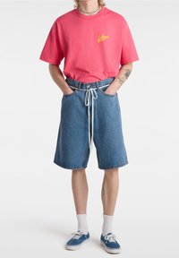 Pink cotton t-shirt with a yellow logo, paired with loose blue denim shorts featuring an adjustable drawstring and cuffed hem.