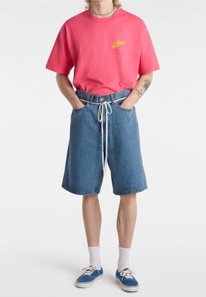 T-shirt en coton rose avec un logo jaune, associé à un short en denim bleu ample avec un cordon de serrage réglable et un ourlet retroussé.