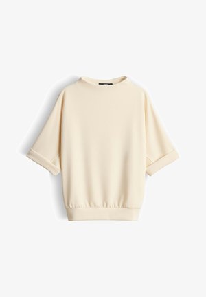 Roomkleurig shirt met korte mouwen, opgerolde manchetten, ronde halslijn en elastische zoom, weergegeven tegen een witte achtergrond.