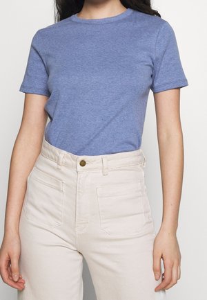 Osoba ubrana w gładki niebieski t-shirt z krótkim rękawem, wpuszczony w wysokowalne, kremowe dżinsy z przednimi kieszeniami naszywanymi.