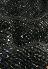Nærbillede af sort strikket stof med sølvtråde og små reflekterende perler spredt rundt omkring.
