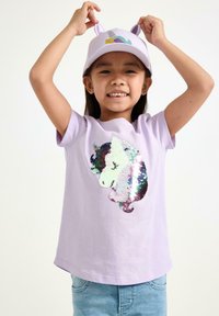 Lavendelfärgad t-shirt med design av en paljettförsedd enhörning. Mjukt bomullstyg, kortärmad, ihop med en ljuslila keps med öron och detaljer.