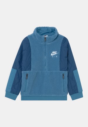 Sudadera azul de forro polar con cuello alto, con cremallera frontal, mangas acolchadas de color azul marino y un bolsillo delantero con cremalleras. Logo de Nike presente.