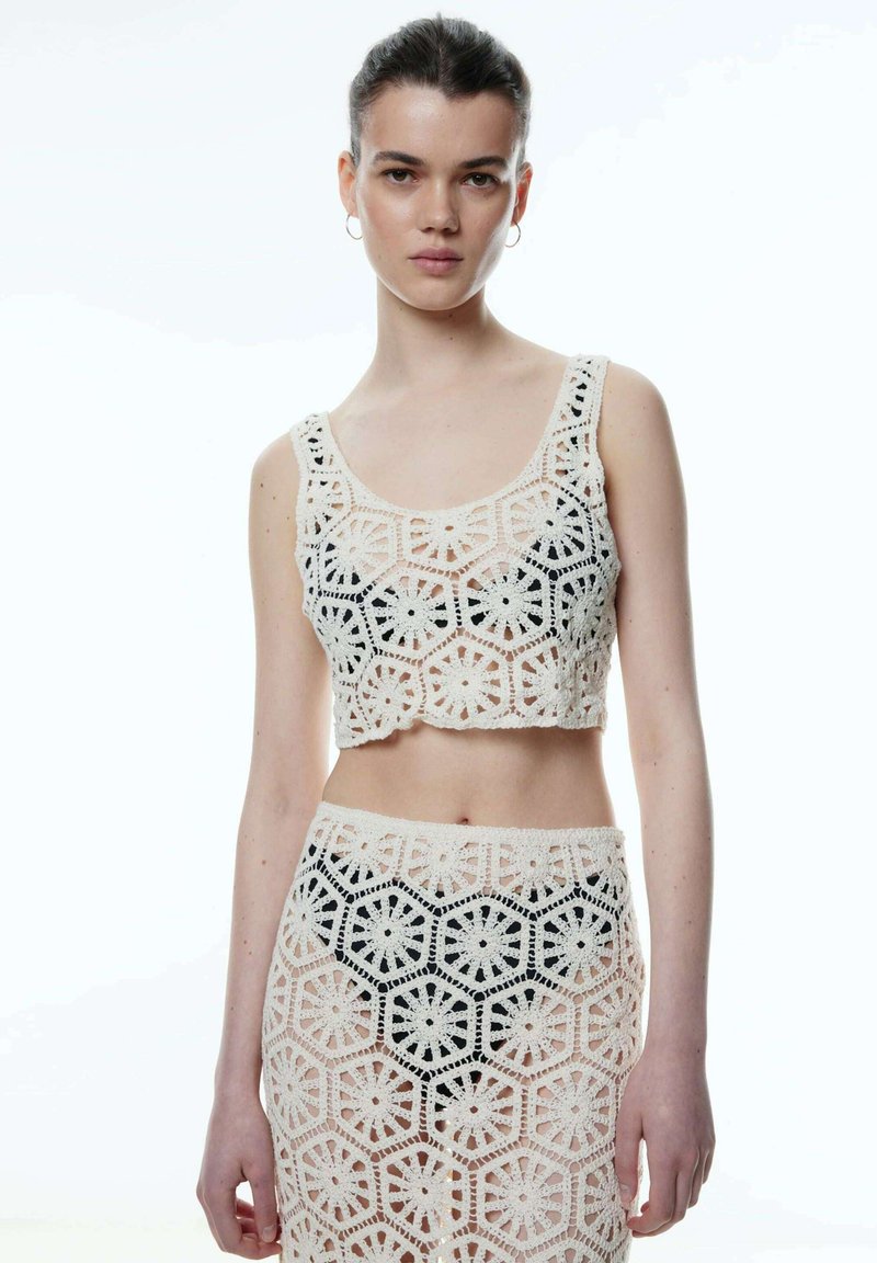 Gehaakte crop top en rok set in crème met hexagonale en bloemige patronen. Kenmerkt een doorzichtig ontwerp en een geribbelde tailleband.
