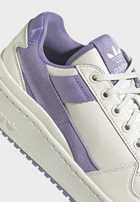 Adidas sneakers featuring a white leather upper with textured purple fabric accents, light grey sole, and white laces.