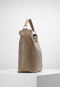 Bolso de cuero topo con una forma estructurada, que cuenta con un asa superior y un sutil acento de logo. Textura suave con detalles de costura visibles.