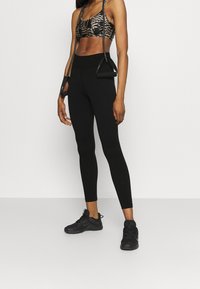 Schwarze Leggings kombiniert mit einem gemusterten Bralette. Die Leggings sind figurbetont und das Bralette hat ein Leopardenmuster.
