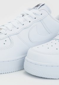 Witte leren sneakers met een gladde textuur, ronde neus, geperforeerde details op het neusvak, en een platte rubberen zool met een patroon op het loopvlak.