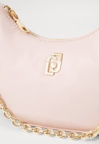 Borsa a tracolla in nylon rosa con catena dorata, accento con logo metallico e chiusura con zip, dalla superficie liscia e forma arrotondata.