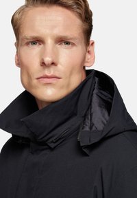 Chaqueta negra de cuello alto con una textura suave y un forro interior brillante. Presenta un cierre con cremallera y un diseño de collar estructurado.