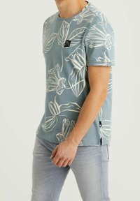 Lyhythihainen, vaaleansiniinen t-paita, jossa on valkoisia kukkakuoseja, pyöreä kaula-aukko ja pieni logo-koristus rinnassa. Sileä rakenne, rento istuvuus.