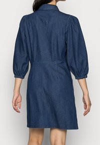 Denim dress with puffed sleeves, button-up collar, elastic waistband, and A-line silhouette, in a dark blue wash. Subtle back yoke detail.