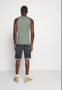 Harmaa toppi, tummat farkkushortsit käännetyillä lahkeilla ja beige korkeakorkoiset lenkkarit. Shortseissa on kaksi takataskua ja haalistunut pinta.