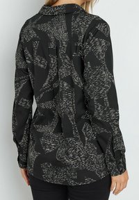 Schwarzes Langarmshirt mit einem hochkontrastierenden abstrakten Muster in Weiß, mit Kragen, knöpfbaren Manschetten und einer lockeren Passform.