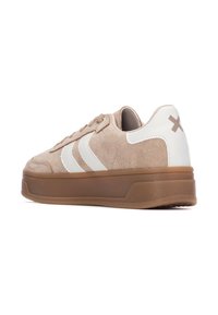 Sneaker in suede beige con dettagli in pelle bianca, caratterizzati da due strisce bianche, una suola spessa marrone e un piccolo logo sul tallone.