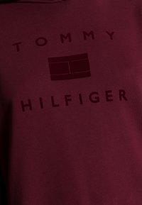 Burgundská mikina s kapucí s vyraženým textem a logem "TOMMY HILFIGER". Hladký bavlněný materiál s jemnou texturou, ležérní design.
