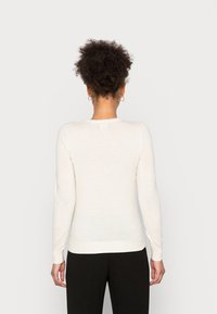 Pull blanc à manches longues avec un col rond, des poignets côtelés et une texture douce ; associé à un pantalon noir, vu de l'arrière.