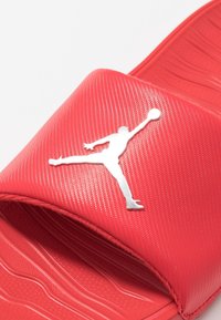 Infradito rossi con parte superiore texturizzata e logo Jordan argentato. La suola presenta un motivo a onde per grip e comfort.