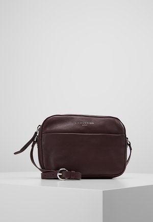 Sac bandoulière en cuir marron foncé avec poche avant et sangle réglable, marqué "Liebeskind Berlin" sur une surface lisse.