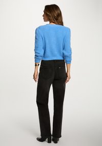Maglione lavorato a maglia blu chiaro con maniche testurizzate, abbinato a jeans neri a vita alta e stivali neri con tacco. La vista posteriore mostra una silhouette aderente.