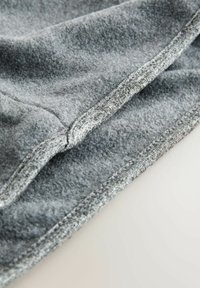 Szürke szövet, puha, textúrált felülettel; lapos varratokkal és tiszta élkezeléssel rendelkezik. A közeli nézet kiemeli az anyag részleteit.