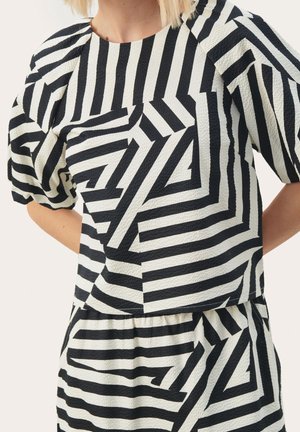 Femme portant un haut à manches courtes à rayures géométriques noires et blanches et une jupe assortie en tissu texturé.