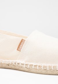 Espadrilles aus Baumwollcanvas in Off-White mit einer genähten Jutesohle und einem kleinen braunen Markenetikett. Runde Zehenpartie und minimalistisches Design.