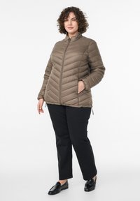 Hnedá prešívaná bunda s vzorom rybej kosti, vysokým golierom, bočnými vreckami a elastickými manžetami. Nosená s čiernymi nohavicami a čiernymi mokasínami.