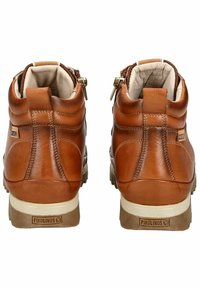 Bottes montantes en cuir marron avec une finition texturée, dotées d'une accent de fermeture éclair et de semelles en caoutchouc blanc. Logo "Pikolinos" à l'arrière.