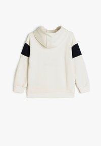 Felpa con cappuccio in crema con dettagli in tessuto nero sulle maniche. Presenta una texture morbida, polsini a coste e un design a vestibilità rilassata.