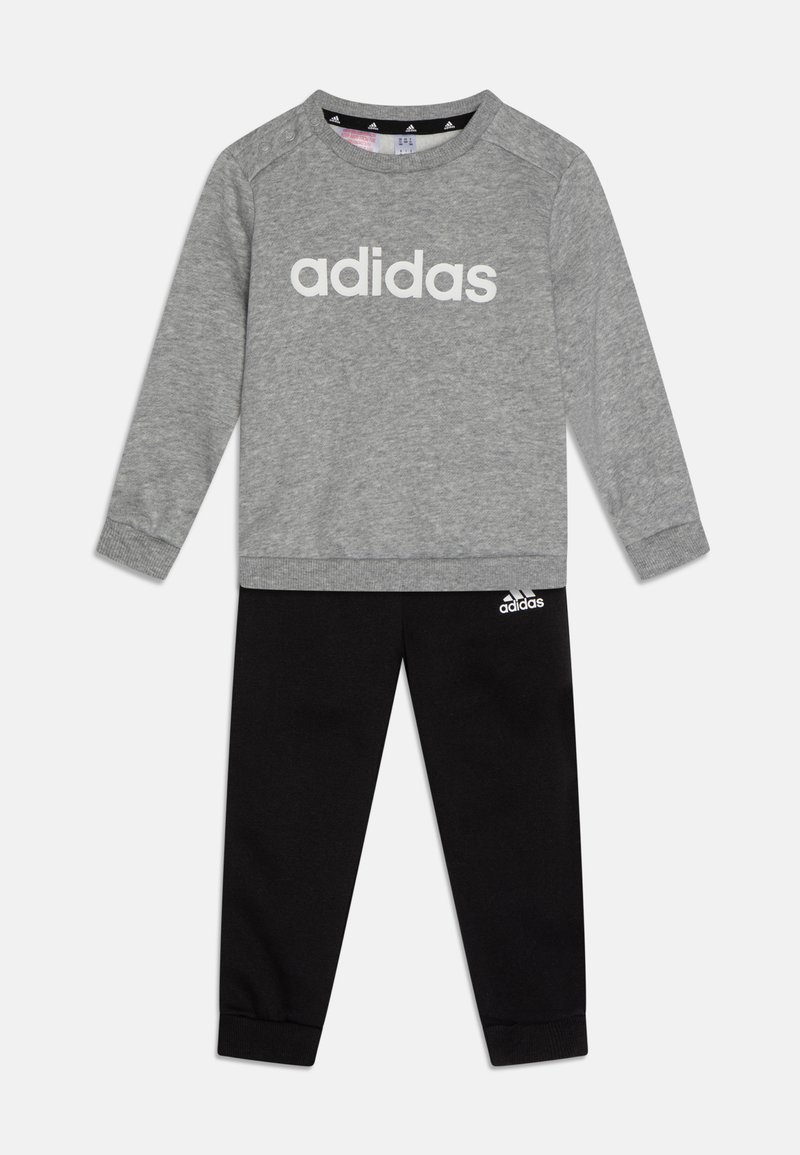 Pilka džemperis su baltu "adidas" logotipu, derinamas su juodomis sportinėmis kelnėmis su mažuoju baltu logotipu. Abu drabužiai turi minkštą, medvilninę tekstūrą.