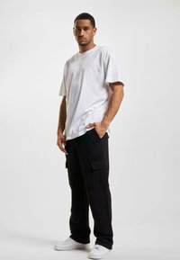 Tricou alb din bumbac cu decolteu rotund, asortat cu pantaloni cargo negri care au buzunare laterale și o croială lejeră, accentuați de adidași albi.