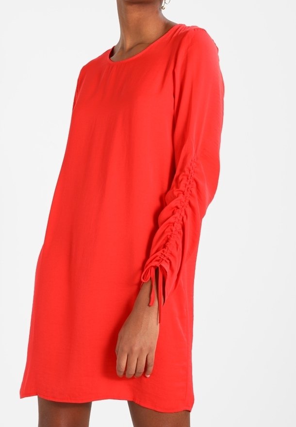 Robe rouge à manches longues avec des détails froncés le long des bras. Fabriquée en tissu léger, elle présente une coupe décontractée et un col rond.