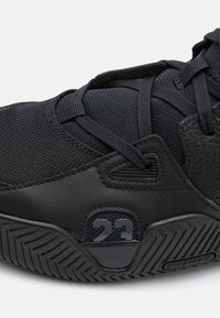 Gros plan d'une chaussure de sport noire montrant un tissu en mesh, des lacets, une semelle texturée et le numéro 23 sur le côté.
