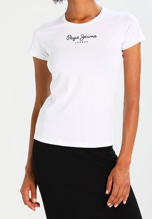 Mujer con una camiseta ajustada blanca de Pepe Jeans London y una falda negra, de pie con una mano apoyada en la cintura.