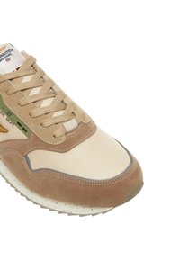 Sneaker beige con materiali in pelle scamosciata e mesh, caratterizzata da un design strutturato, lacci evidenti, suola maculata e etichetta accento verde.