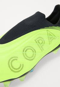 Lys grøn fodboldstøvle med sort tekstiloverdel, struktureret design og perforeret "COPA" skrifttype. Har formede knopper for trækkraft.