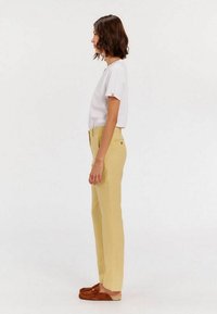 Un pantalon droit jaune clair avec une fermeture à bouton, associé à une chemise blanche avec des rayures rouges sur les manches.