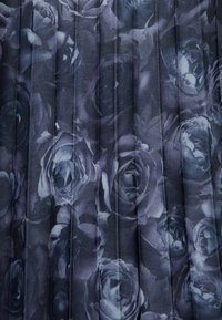 Tissu foncé présentant un motif plissé, orné de roses grises et noires, créant un motif floral texturé sur toute la surface.