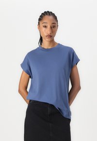 Blaues Kurzarm-T-Shirt aus weichem Stoff, mit rundem Halsausschnitt und lockerer Passform. Kombiniert mit einem schwarzen Rock.