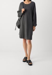 Abito grigio oversize in maglia con scollo rotondo e maniche lunghe, abbinato a sandali platform neri e a una borsa nera.