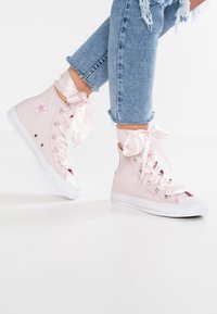 Rosa canvas högskor med satinband, gummitå och vit sula. Har logotypmärke på den yttre sidan.