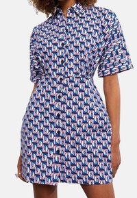 Abito camicia a maniche corte in cotone, con un motivo geometrico di forme rosa, blu e bianche, dotato di una chiusura frontale con bottoni e una vita aderente.