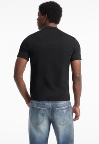Sort kortærmet t-shirt med rund hals, lavet af bomuld, vist på en person iført falmede blå jeans med baglommer.