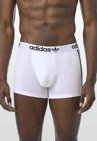 Weiße Baumwoll-Boxershorts mit einem schwarzen elastischen Bund, der das "adidas"-Logo und drei schwarze Streifen an den Seiten zeigt.